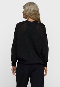 Zwarte, loszittende trui met een gestructureerde breisel, brede mouwen en een iets cropped achterkant. Glad materiaal en eenvoudig ontwerp.