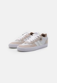 Sneaker basse in suede beige e pelle bianca con dettagli perforati. Suola in gomma con grip texturizzato, chiusura con lacci e branding discreto.