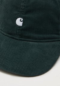 Ciemnozielona czapka baseballowa z koronką, z zakrzywionym daszkiem i małym białym haftowanym logo na przednim panelu.