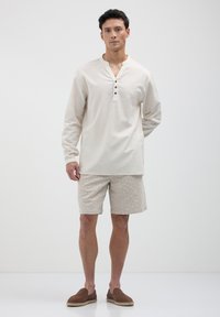 Helle beige Langarmshirt mit einem geknöpften Henley-Ausschnitt. Kombiniert mit strukturierten beigen Shorts und braunen Slipper-Espadrilles.