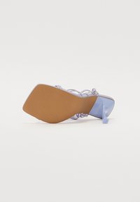 Sandale à talons hauts lavande avec un orteil carré, des fines lanières, une finition lisse et une semelle marron avec un motif texturé.