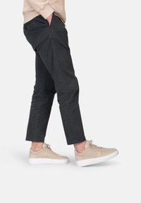 Zapatillas de ante beige con una parte superior texturizada y suela de goma blanca, combinadas con pantalones ajustados gris oscuro. Diseño minimalista con cordones.