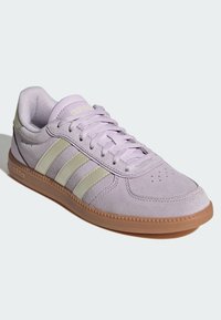 Fioletowy zamszowy sneaker z trzema jasnooliwkowymi paskami, teksturowaną powierzchnią, sznurowanym designem i brązową gumową podeszwą. Posiada perforacje na czubku.