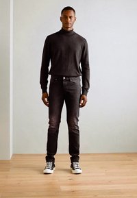 Pull encolure ras du cou noir, jean foncé et baskets noires. Texture lisse et design ajusté avec des détails subtils sur le jean.
