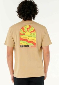 Tan katoen T-shirt met een kleurrijke zonsondergangafdruk en golven, en de tekst "RIP CURL SINCE SIXTY NINE" op de achterkant.
