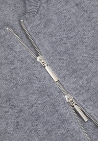 Szary sweter robiony na drutach z srebrnym zamkiem z przodu. Posiada ściągacz na dekolcie oraz gładki, teksturowany materiał.