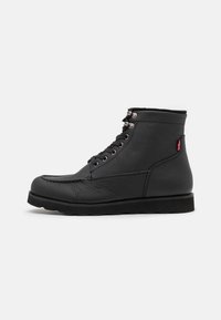 Bottines en cuir noir, avec un bout rond, un design à lacets et une surface texturée. Elles présentent des œillets en métal et une semelle noire robuste.