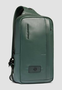 Donkergroene leren rugzak met een gladde textuur, subtiele stiksels, ritsafsluiting en een gebrandmerkt accent. Compact en rechthoekig van vorm.