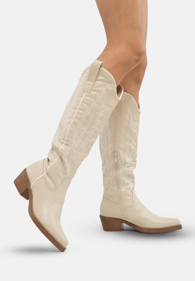 Botas western de cuero color crema hasta la rodilla, con bordados de hojas, cremallera lateral y tacón grueso. Textura suave con puntas puntiagudas.