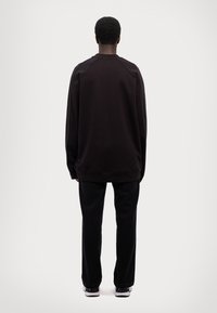 Crni oversized dukserica s dugim rukavima, izrađena od mekanog materijala, i odgovarajuće crne ravne hlače. Minimalistički dizajn, bez vidljivih uzoraka.