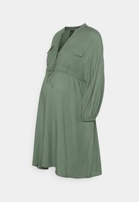 Vestido de maternidade em verde sálvia, com decote em V, dois bolsos no peito, cintura com cordão ajustável e mangas longas bufantes. Feito de tecido leve.