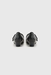 Black leather heels with a low block heel, rounded toe, and decorative bow detail on the side. Smooth texture and simple design.