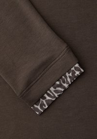 Bruine lange mouw stof met een gladde textuur; de mouwboord heeft een patroon in grijs en wit, met een contrasterend detail.