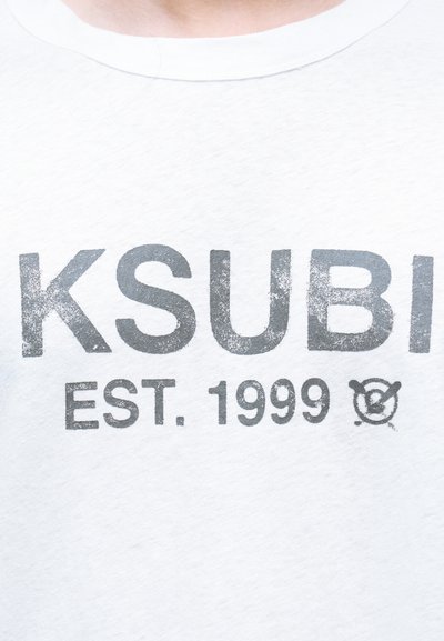 Λευκό βαμβακερό t-shirt με μεγάλο, ξεθωριασμένο γκρι τύπωμα της λέξης "KSUBI" και "EST. 1999", καθώς και ένα μικρό γραφικό στοιχείο από κάτω.