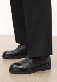 Pantofi din piele neagră cu un finisaj texturat, vârful rotund, vârful întărit și o talpă robustă. Purtați cu pantaloni negri, croiți.