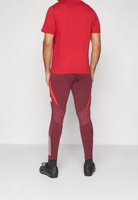 Rode t-shirt met korte mouwen, gecombineerd met bordeauxrode sportleggingen met rode accenten en witte zijstrepen. Gekocht met zwarte sportschoenen.