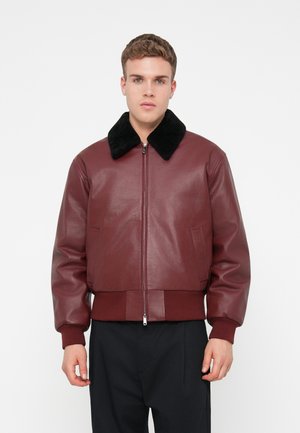 Burgundská kožená bunda s černým umělým kožešinovým límcem, zapínání na zip a žebrovanými lemy a manžetami; obsahuje postranní kapsy a hladký povrch.