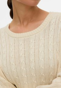 Jasno beżowy sweter dzianinowy z okrągłym dekoltem, ozdobiony teksturowymi wzorami w warkocze i wykonany z miękkiej, grubej przędzy.