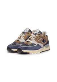 Un paio di sneaker basse con pannelli in camoscio e rete blu, marrone e beige, suola bianca macchiata e lacci beige, inclinati a destra su uno sfondo bianco.