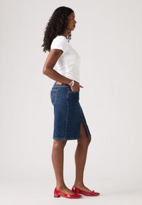 Gonna a tubino di denim con spacco frontale, abbinata a una t-shirt bianca aderente. Completata da ballerine rosse in vernice. Design semplice e colori classici.