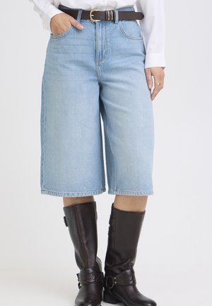 Jasnoniebieskie denimowe szorty do kolan noszone z białą koszulą, brązowym paskiem i ciemnobrązowymi skórzanymi kozakami za kolano.