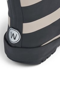 Botte en caoutchouc noire et beige avec des rayures horizontales ; présente un logo rond accentuant le côté, semelles texturées pour une bonne adhérence.