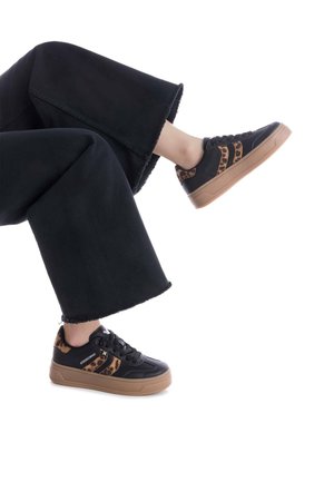 Zapatillas negras y marrones con un acento de estampado de leopardo, parte superior de cuero texturizado, suela de goma y diseño de cordones; combinadas con pantalones anchos negros.