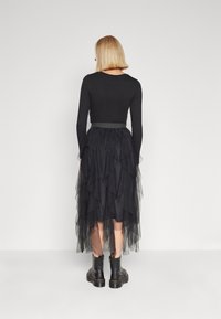 Black layered tulle skirt with ruffled edges, paired with a form-fitting long-sleeve top and black ankle boots with a chunky sole.
