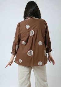 Bruine geborduurde blouse met bloemmotieven, lange mouwen en een gerimpelde halslijn, gecombineerd met lichte broek.