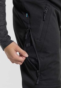 Black pants with a zippered pocket, featuring mesh lining and adjustable straps. Small Swedish flag detail on the side. Sleek, athletic design.
