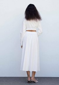 Chemise blanche courte à manches longues et jupe blanche fluide taille haute. La jupe dispose d'une taille élastique pour plus de confort.