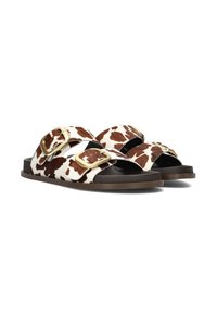 Bruine en witte koeienprint sandalen met twee brede banden, gouden gespaccenten en een bruine platte zool. Gladde textuur en open ontwerp.