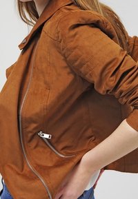 Bruine suède jas met een slim fit ontwerp, horizontale gewatteerde textuur op de schouders en een zilveren rits op het zijvak.