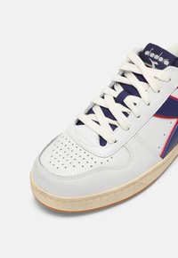 Baskets en cuir blanc avec accents bleu marine et rouge, bout rond, empeigne perforée, lacets crème et semelle extérieure en caoutchouc texturé.