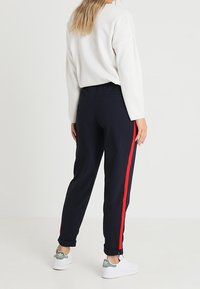 Joggers de color navy con una franja lateral roja, cinturilla elástica y puños. Combinados con una camiseta blanca de manga larga y zapatillas blancas.