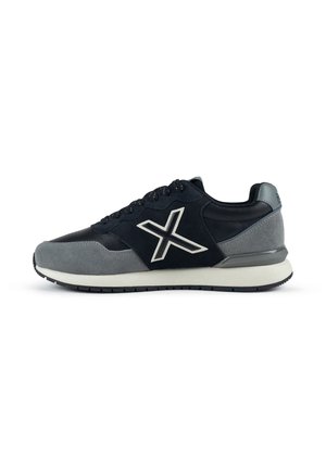 Baskets basses noires et grises avec une semelle blanche et un grand logo blanc "X" sur le côté.
