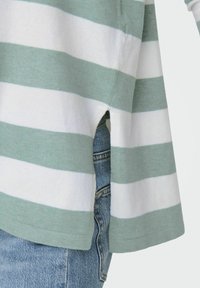 Pull rayé vert clair et blanc, doté d'une fente latérale, fabriqué en tissu doux, avec des détails d'ourlet incurvé, associé à un short en denim.