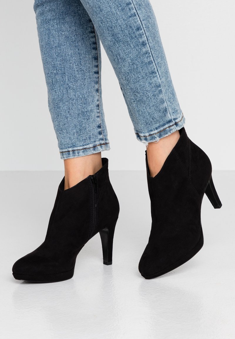 Bottines en daim noir avec un bout pointu, une fermeture éclair latérale et un talon haut élancé. Portées avec un jean court bleu clair.