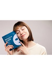 Patchology Beauty Sleep hydrogelmaske. Blå emballage med hvide detaljer. Model holder pakken tæt ved sit ansigt, iført en cremet skjorte.