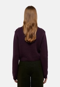 Pull en tricot violet foncé avec un design court, des poignets côtelés et une texture douce. Présenté de dos sur fond blanc.