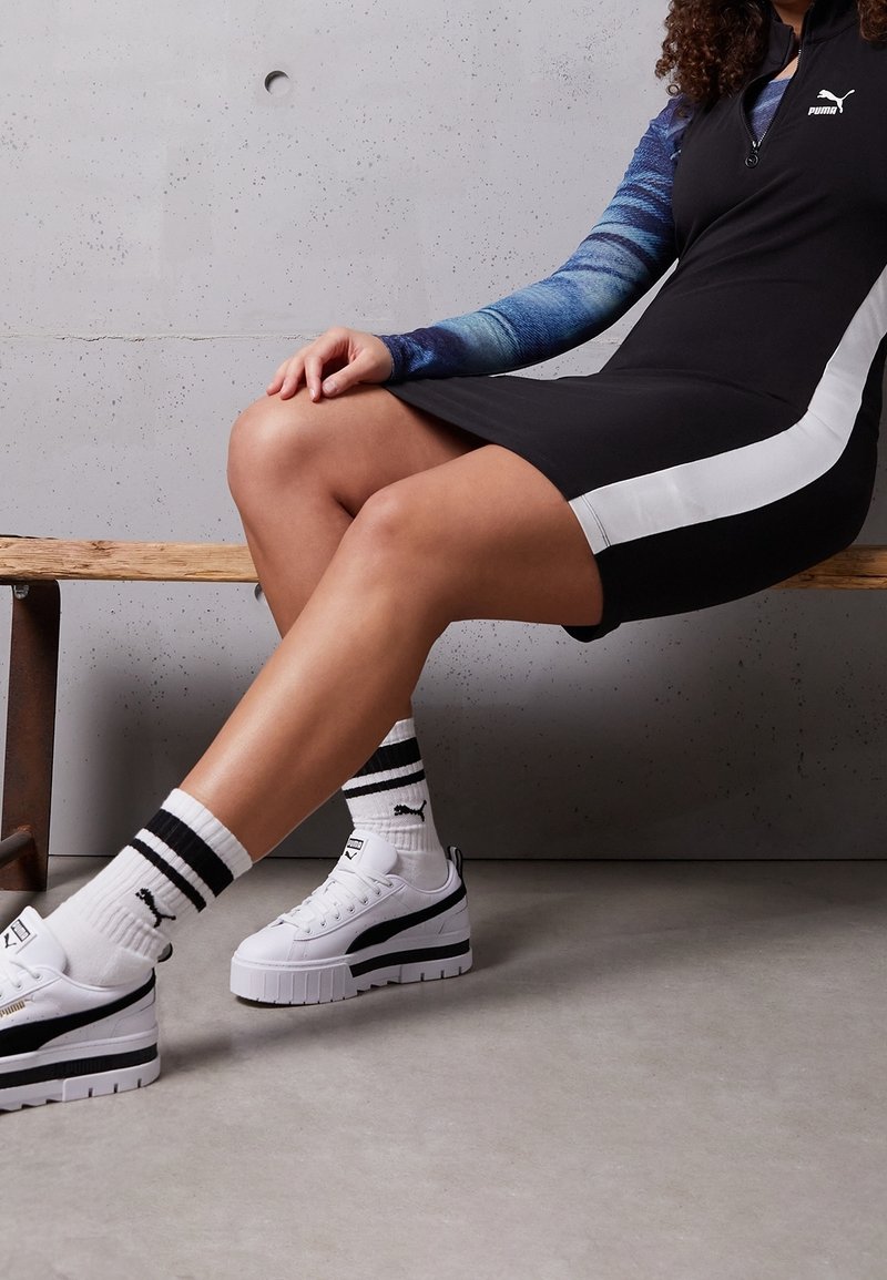 Robe noire avec des bandes latérales blanches, haut à manches longues bleu, baskets blanches à semelles épaisses avec accents noirs, et chaussettes de sport rayées.