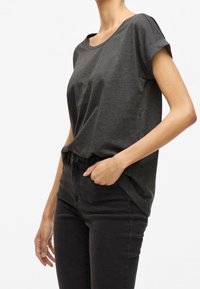 T-shirt gris foncé à manches courtes avec un col rond, une coupe décontractée et des détails aux revers roulés, associé à un jean noir taille haute.