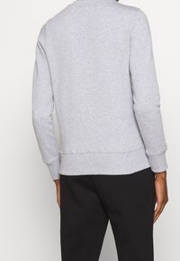 Person wearing a light grey long-sleeve sweatshirt and black pants, shown from the back against a plain background.