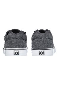 Gray fabric sneakers with a textured finish, white rubber sole, and black logo patch on the heel. Low-top design with flat laces.