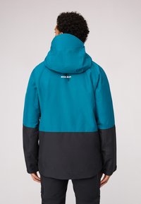 Wasserdichte Jacke mit einem türkisfarbenen oberen Abschnitt und einem schwarzen unteren Abschnitt. Enthält eine Kapuze und ein Logo auf der Rückseite. Glatte Textur.