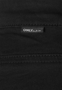 Tejido de mezclilla negro con costuras visibles. Presenta una pequeña etiqueta con el texto "ONLY", situada en el borde superior. Textura suave.