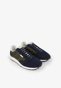 Marineblauwe sneakers met een groen gaaspaneel, witte zool en doodskoplogo. Voorzien van vetersluiting en gestructureerde stofaccenten.