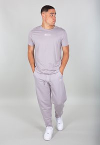 T-shirt in cotone grigio chiaro con collo rotondo e logo sul petto, abbinato a pantaloni della tuta leggeri grigi e sneakers bianche.