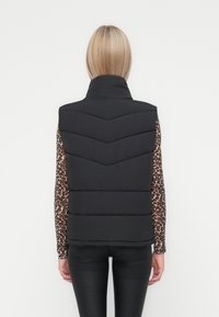 Zwarte puffer vest met een hoge kraag en een chevronstiksels patroon. Draagt over een lange mouwen shirt met luipaardprint, met een aansluitend ontwerp.
