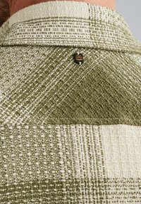 Groen en beige gestoffeerd met een getextureerde weving, met een klein zwart label op de achterkant van de kraag met de tekst "P.M.E Legend."